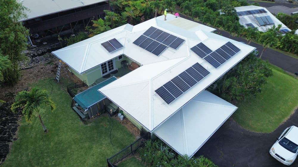 Aerial view of a house with solar panels, surrounded by greenery and driveway.