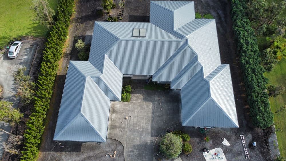 Aerial view of a modern home with multiple roofs and a paved outdoor area.