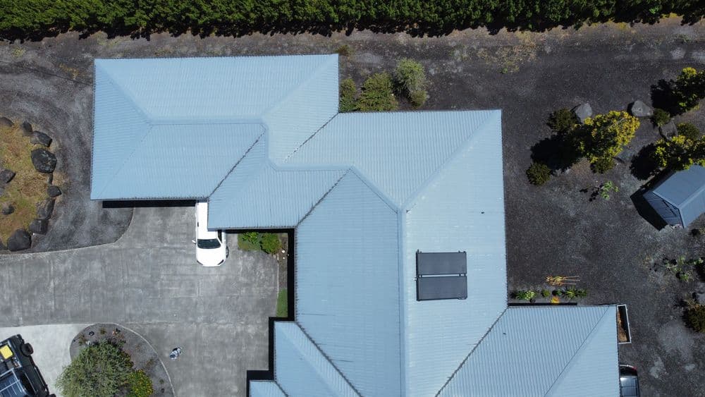 Aerial view of a modern home with a gray metal roof and surrounding landscaped garden.
