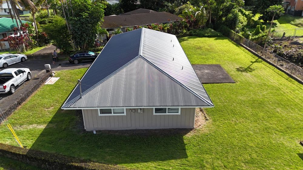 Aerial view of a single-story house with a metal roof and green lawn.