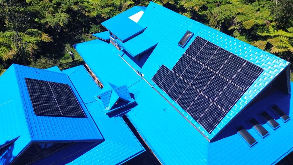 Blue house with solar panels on the roof surrounded by lush greenery. Eco-friendly energy solution.